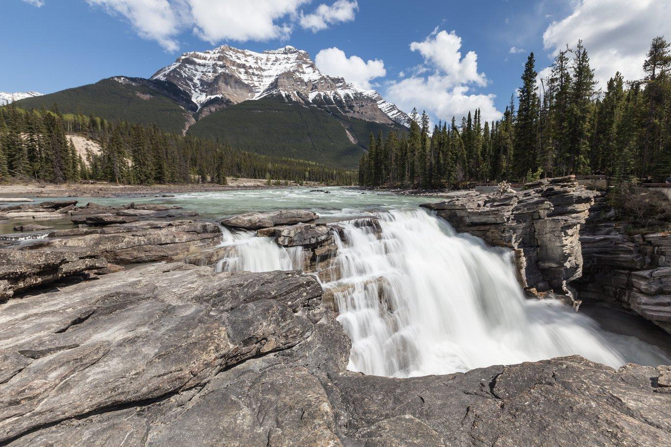 Athabasca Falls pouring through a rock gorge below a snowy peak