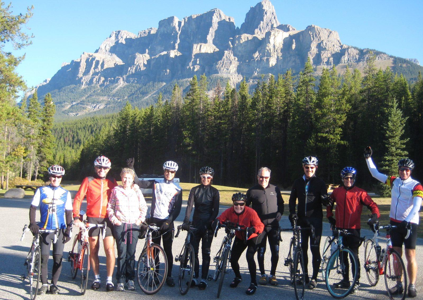 A tour group in cycling gear lined up with their bikes in front of the cliffs of Castle Mountain