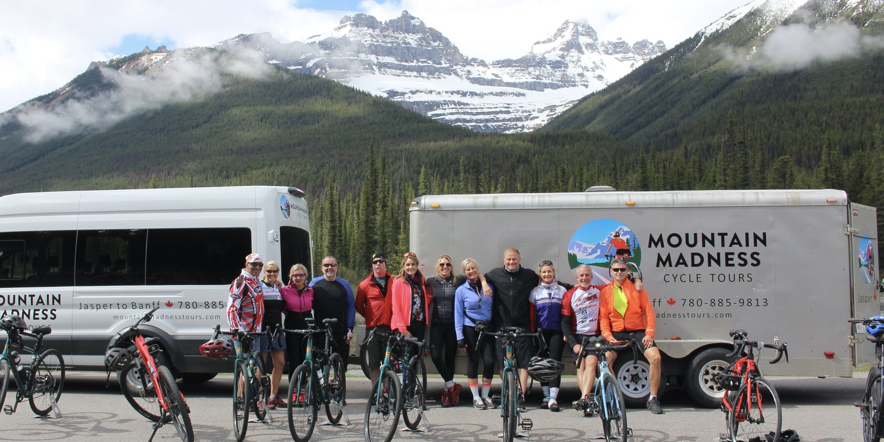 A Mountain Madness tour group with their bikes in front of the support van and bike trailer, snow-capped peaks behind